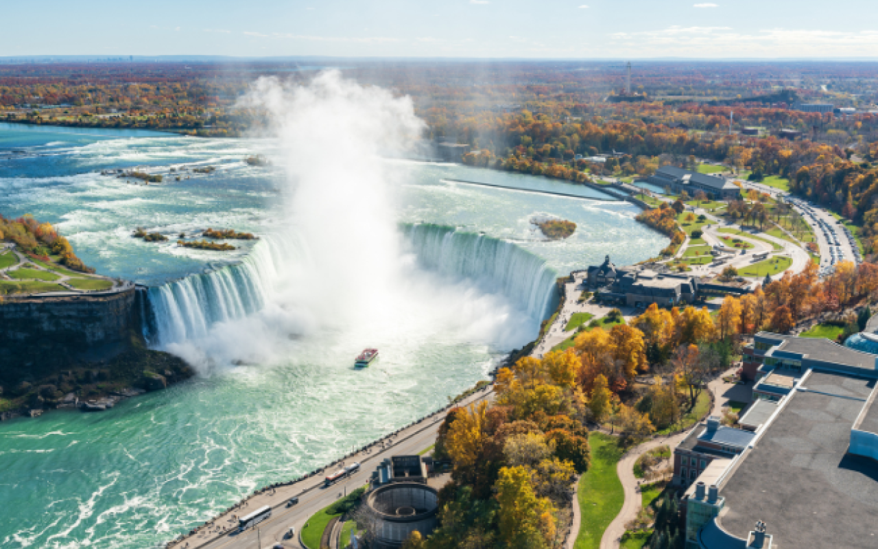 Vista aerea delle Cascate del Niagara in autunno: l'Horseshoe Falls a ferro di cavallo con la nuvola di spruzzi, la barca Maid of the Mist e i boschi colorati sulle due sponde